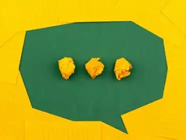 A stylized green speech bubble against a yellow background contains three crumpled yellow paper balls in the center, resembling the "typing" indicator seen in messaging apps.