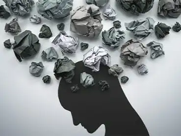 Silhouette of a person's head with crumpled paper balls emerging from the top, symbolizing thoughts or ideas. The paper balls start dark and gradually lighten as they spread outward. The background is a soft gradient of gray.