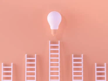 A light bulb floats above five ladders aligned vertically against a peach-colored background. The middle ladder reaches the light bulb, while the others do not. The image represents reaching an idea or insight.