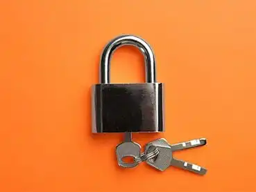 A shiny silver padlock with an attached set of two metal keys on an orange background.